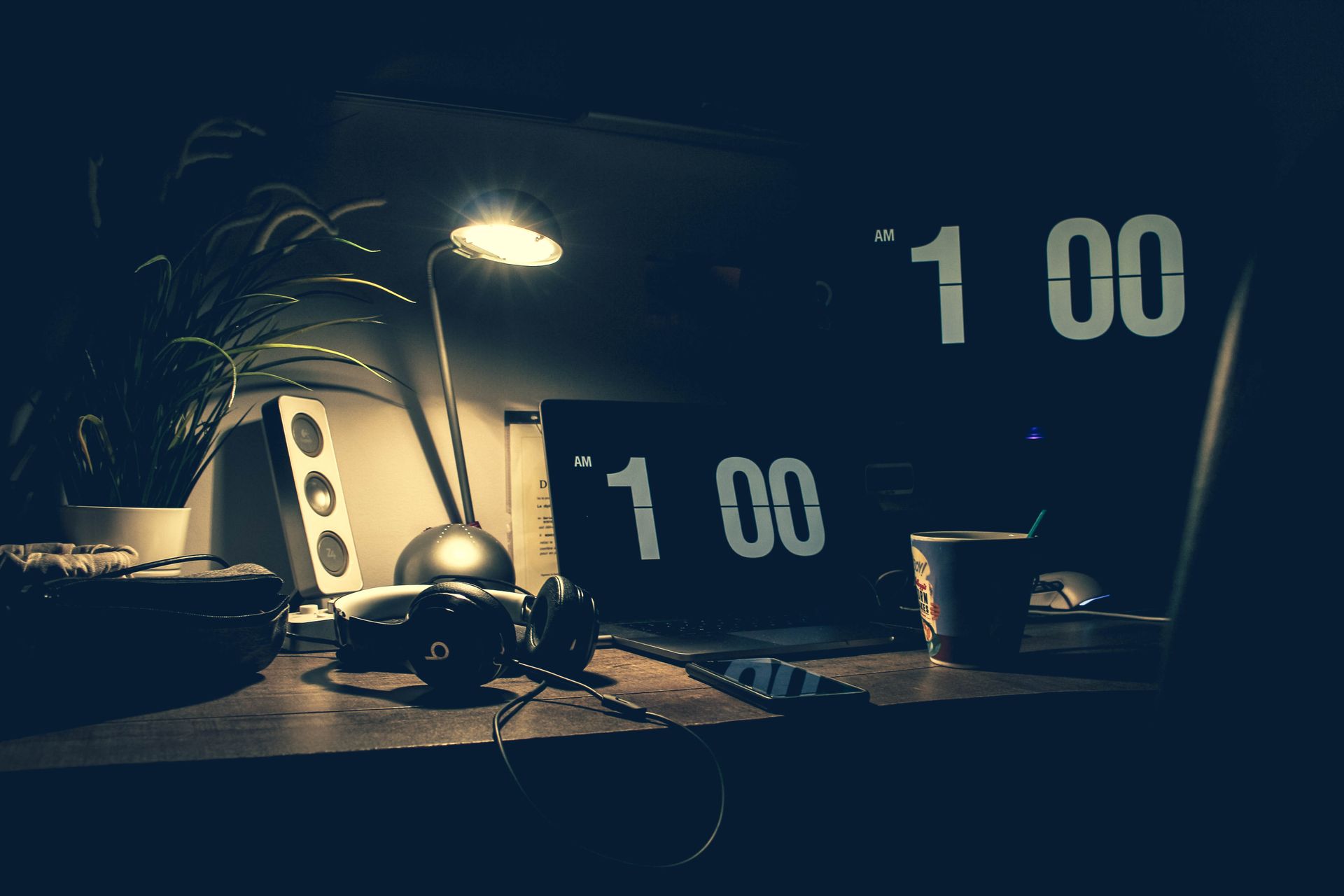 A dark desk at night with a glowing clock showing 1:00